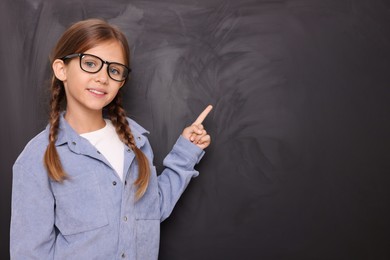 Smiling schoolgirl in glasses pointing at something on blackboard. Space for text