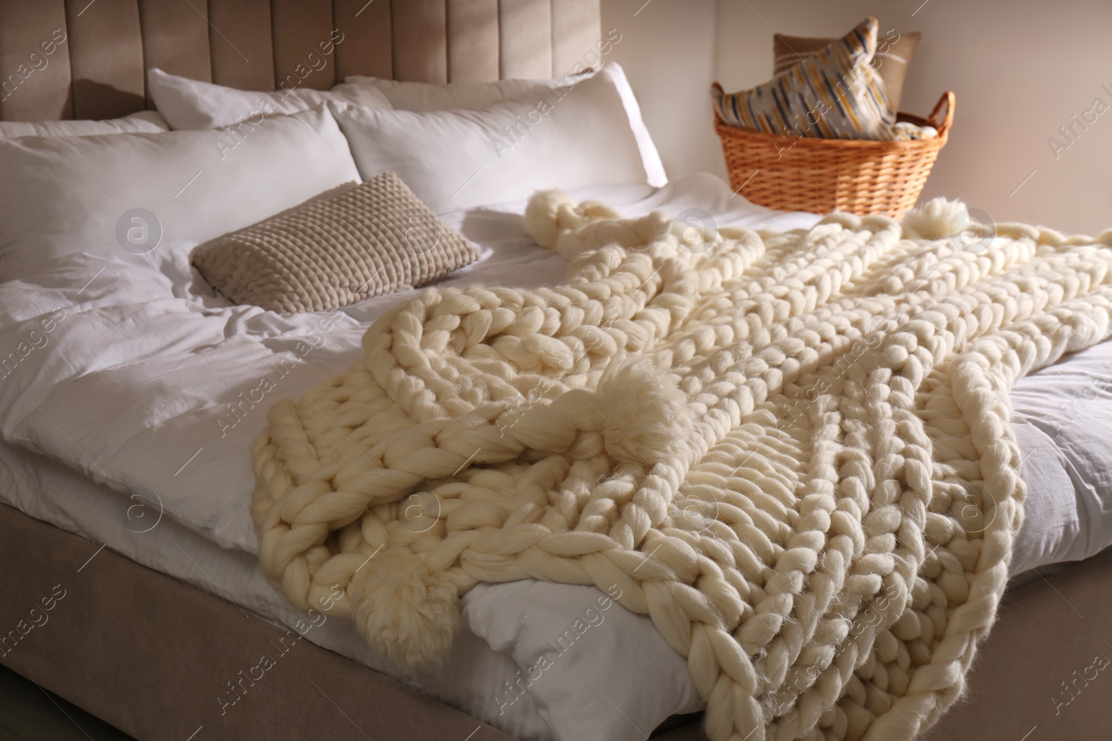 Photo of Bed with white knitted plaid indoors. Interior design