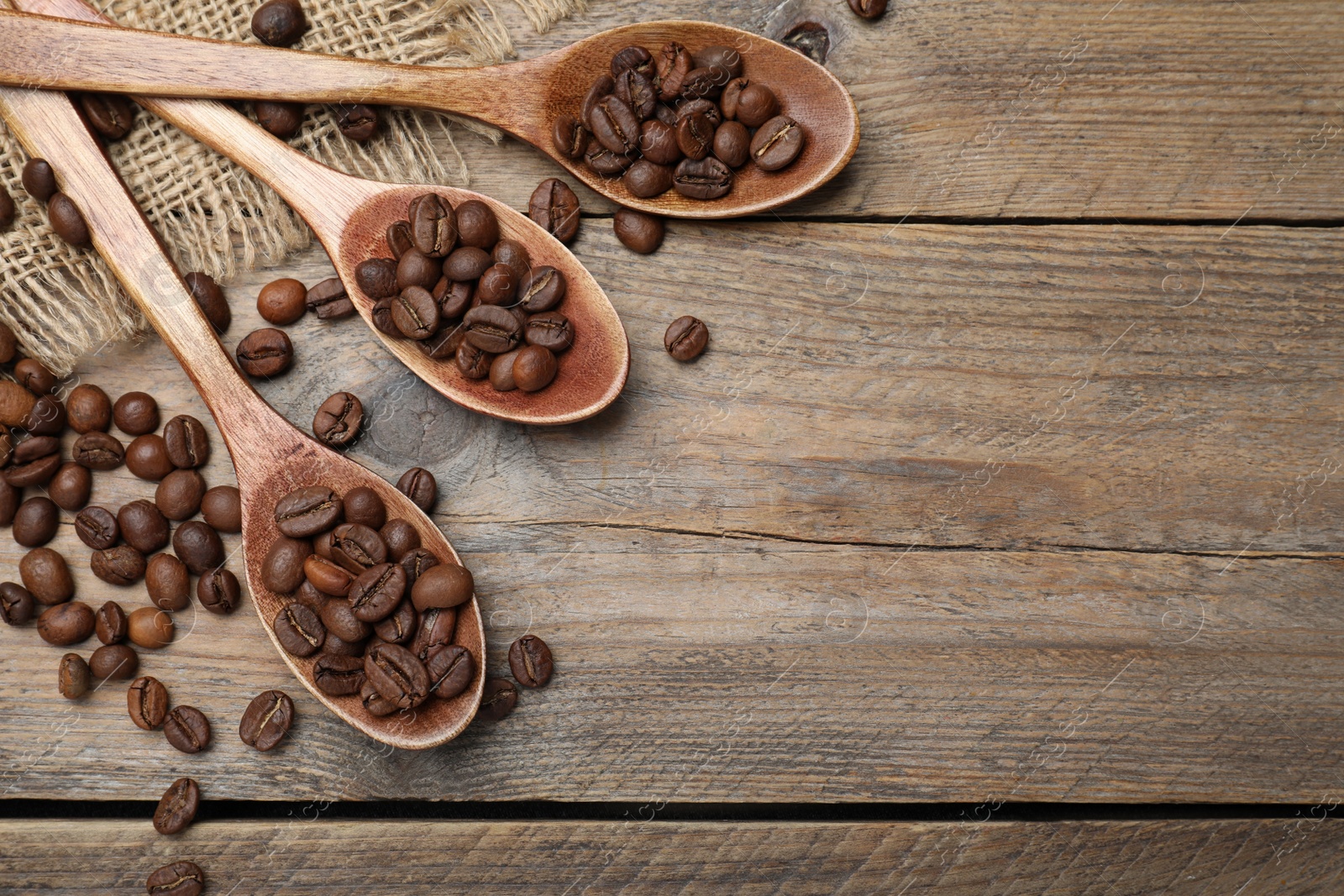 Photo of Spoons with roasted coffee beans on wooden table, flat lay. Space for text