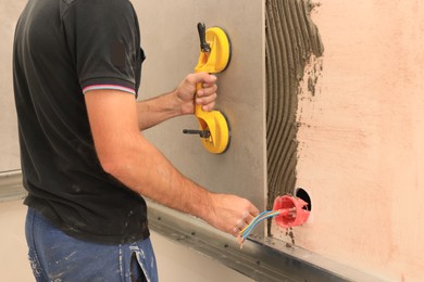 Photo of Worker using suction plate for tile installation indoors, closeup