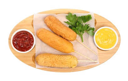 Delicious deep fried corn dogs and sauces isolated on white, top view
