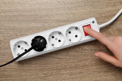 Photo of Woman pressing button of power strip on wooden floor, top view. Electrician's equipment