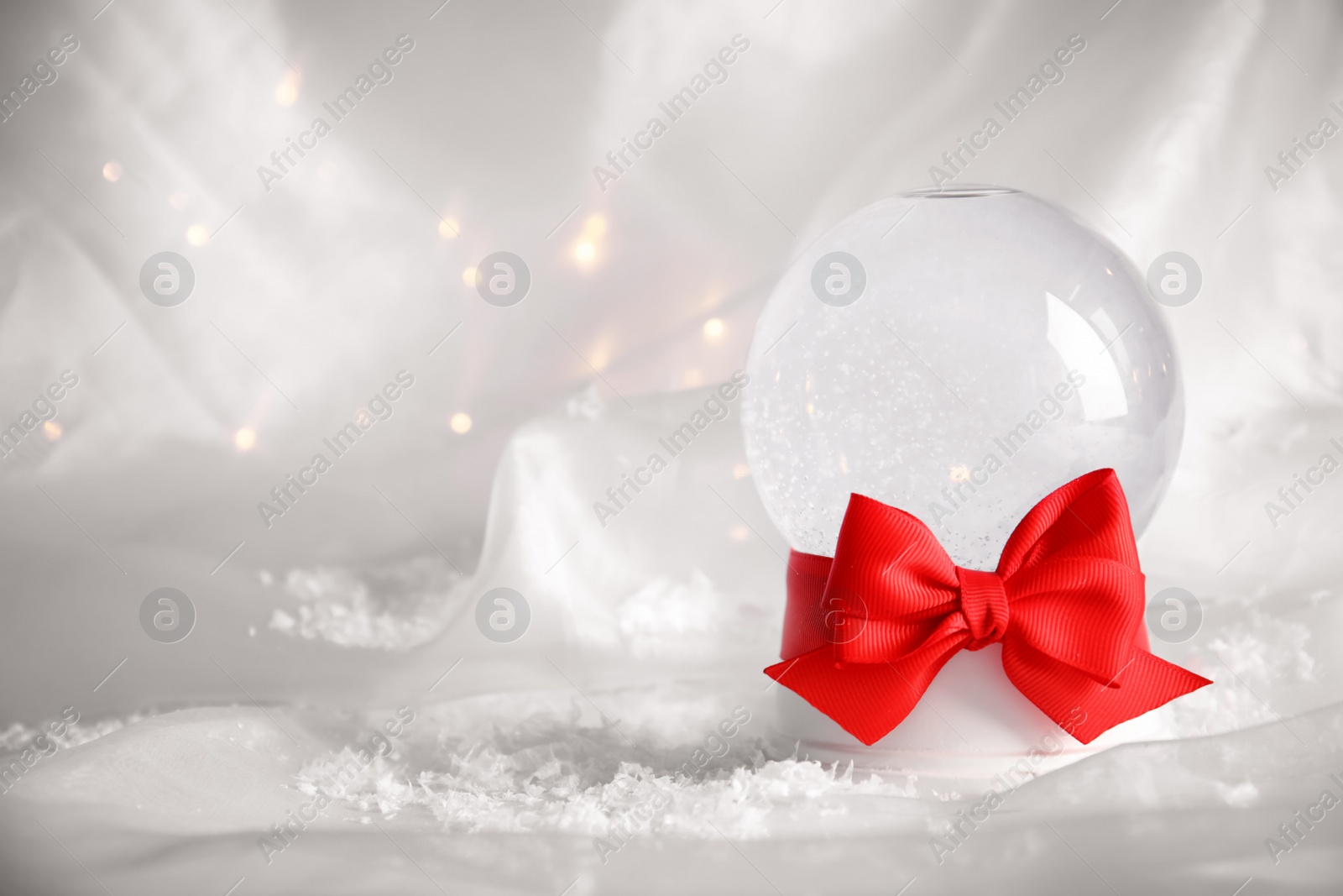 Photo of Empty snow globe with red bow on white fabric. Space for text