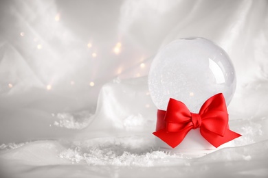 Empty snow globe with red bow on white fabric. Space for text