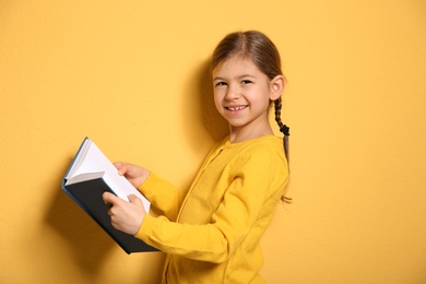 Photo of Cute little girl with book on color background
