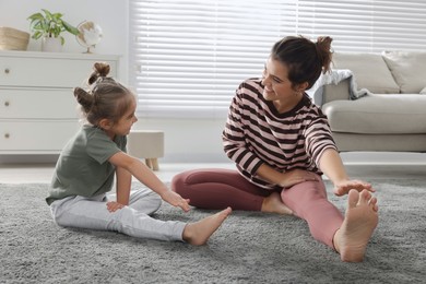 Photo of Young mother and her daughter stretching together at home