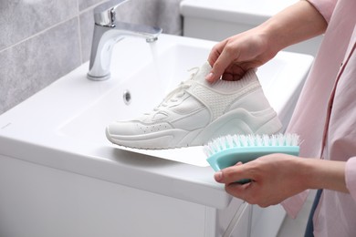 Photo of Woman washing stylish sneakers with brush in sink, closeup