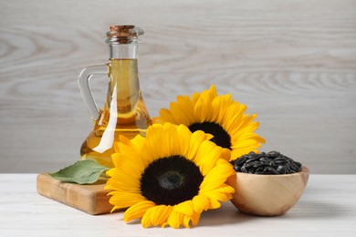 Photo of Sunflower cooking oil, seeds and yellow flowers on white wooden table