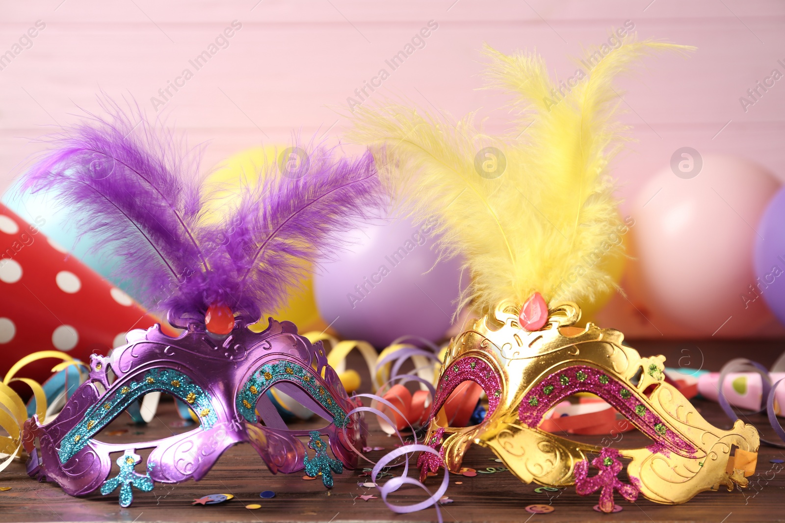 Photo of Beautiful carnival masks and party decor on wooden table, closeup