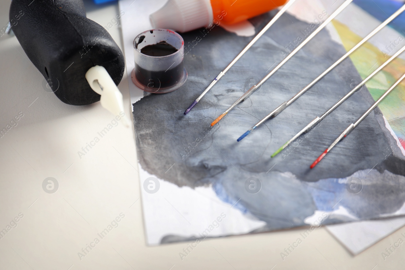 Photo of Tattoo machine, needles, ink and sheets of paper on table