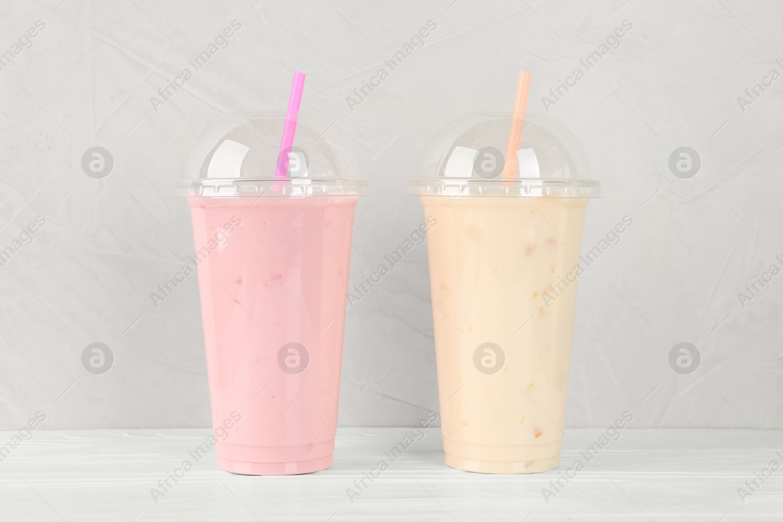 Photo of Plastic cups of different tasty smoothie on white wooden table