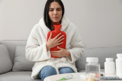 Photo of Ill woman with hot water bottle suffering from cold at home