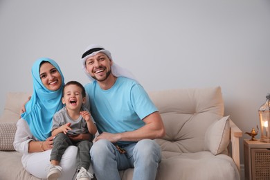 Happy Muslim family on sofa in living room, space for text