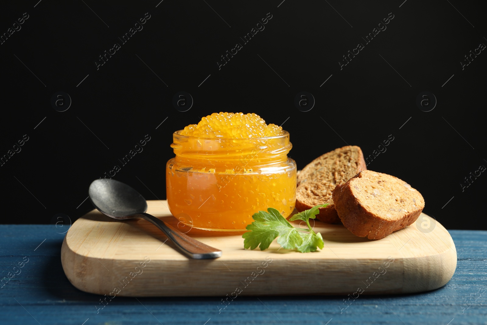 Photo of Fresh pike caviar in glass jar, bread and parsley on blue wooden table, closeup