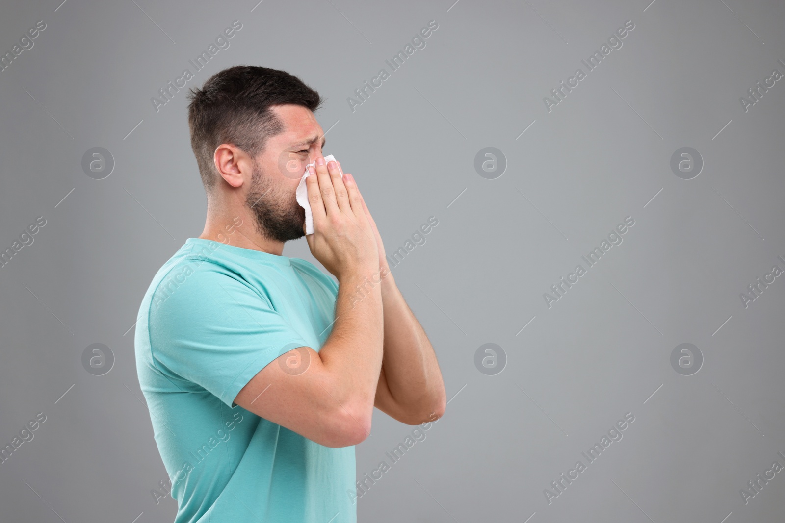 Photo of Allergy symptom. Man sneezing on light grey background. Space for text