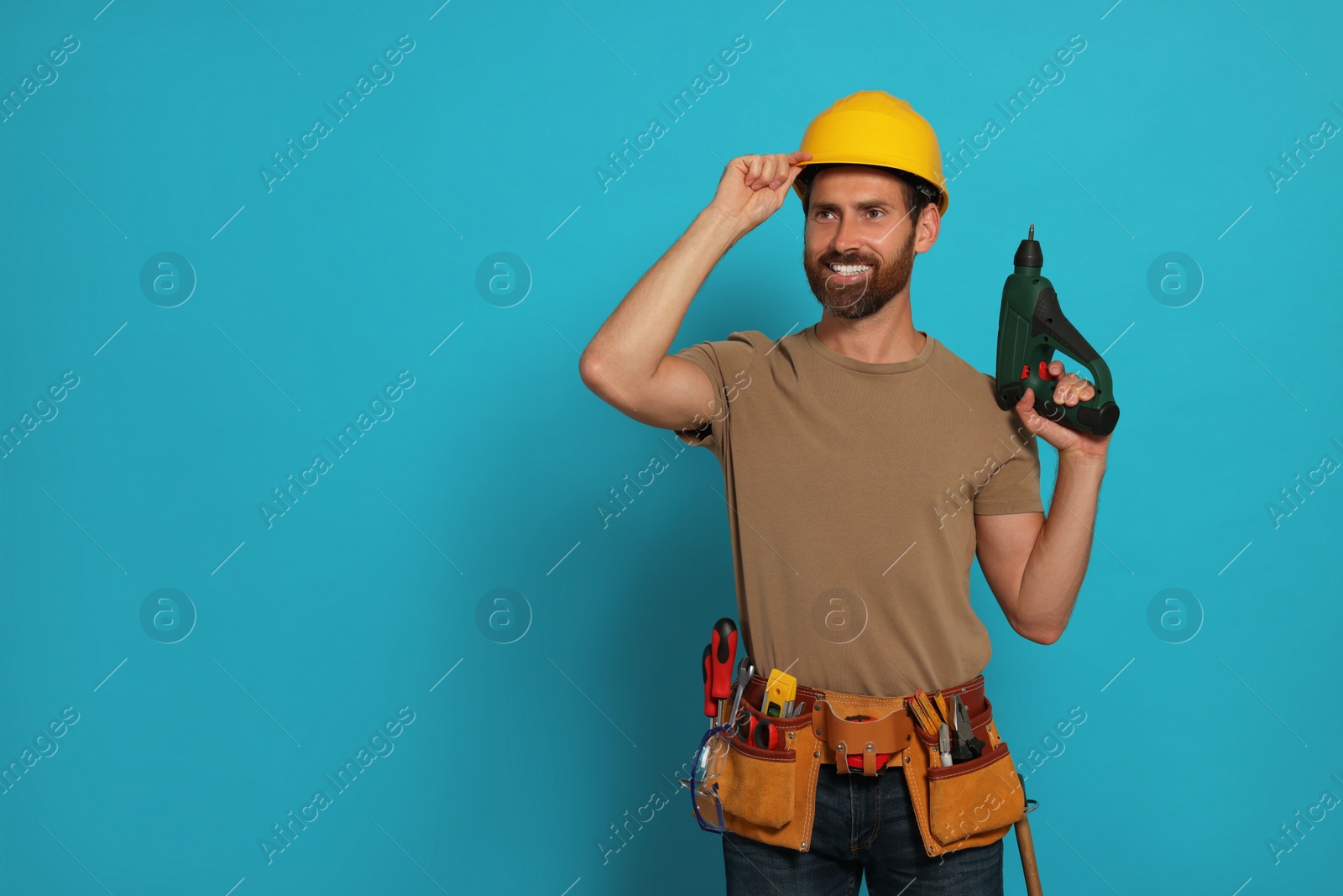 Photo of Professional builder in hard hat with tool belt and power drill on light blue background, space for text