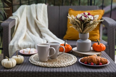 Photo of Rattan table with cups of drink, croissants, cheese and autumn decor on terrace
