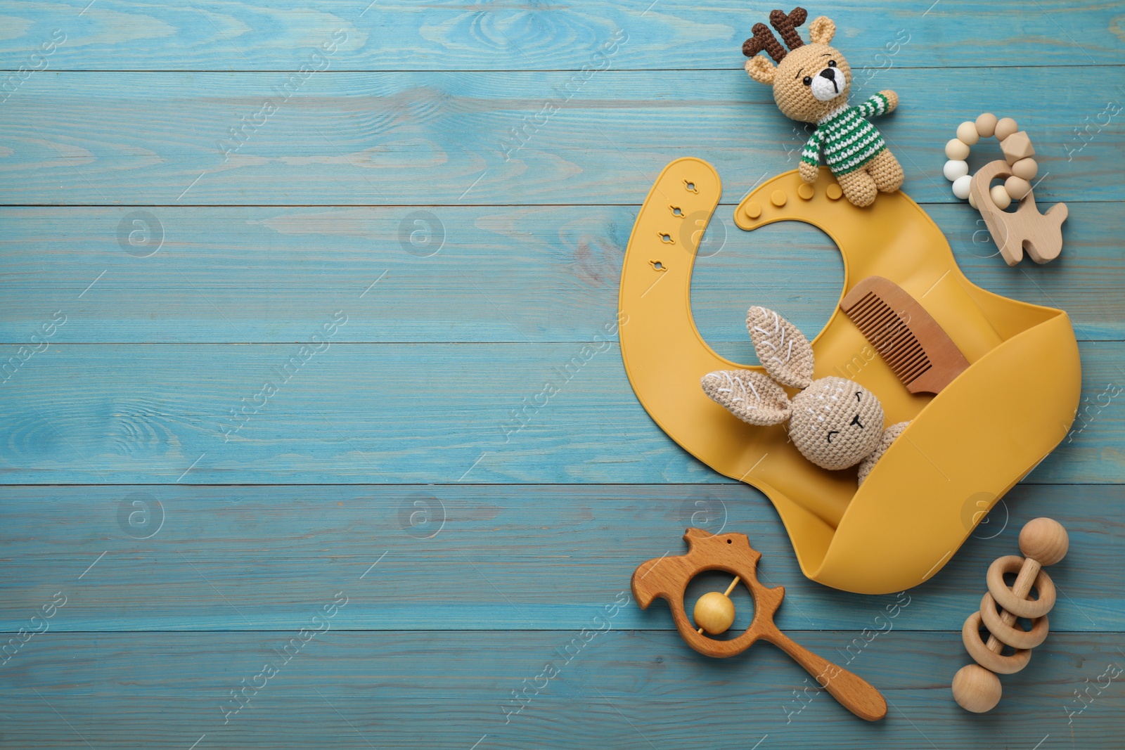 Photo of Flat lay composition with silicone baby bib and toys on light blue wooden background. Space for text