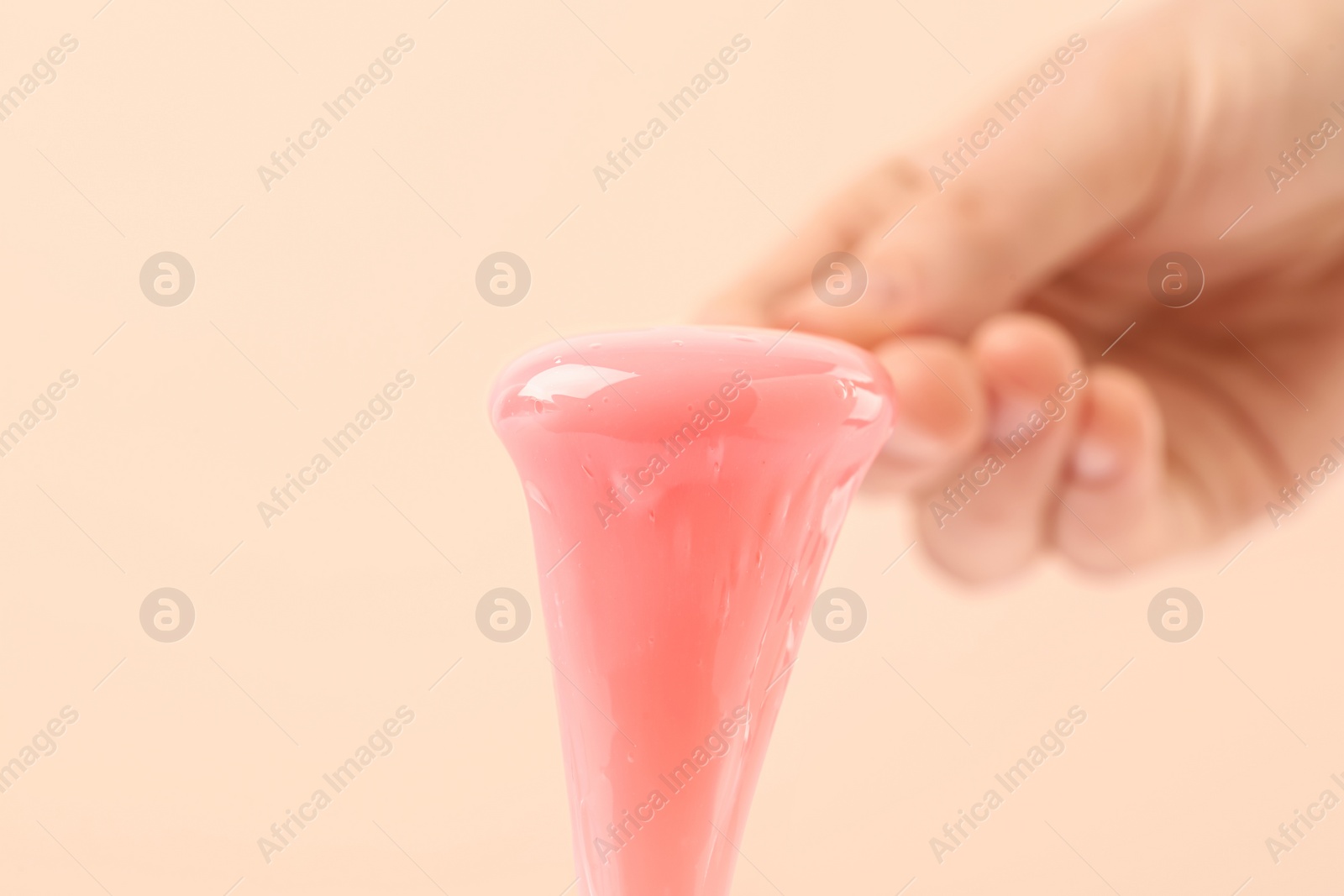 Photo of Woman holding spatula with hot depilatory wax on beige background, closeup