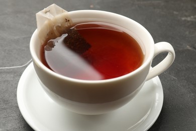 Photo of Tea bag in cup with hot drink on grey textured table, closeup