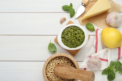 Delicious pesto sauce in bowl and ingredients on white wooden table, flat lay. Space for text