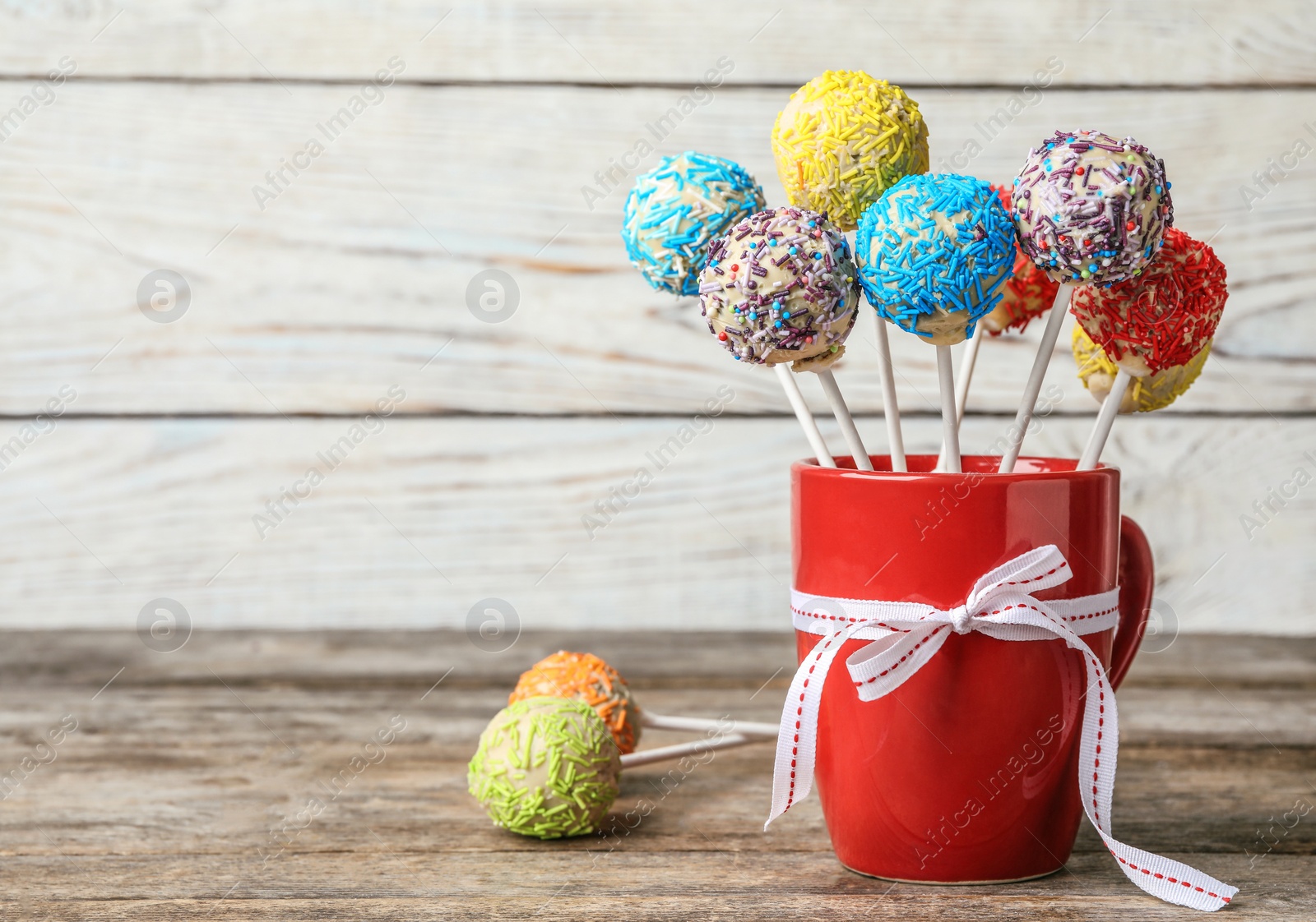 Photo of Cup with bow and yummy colorful cake pops on table. Space for text