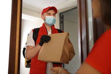 Courier in protective mask and gloves giving order to woman at entrance. Restaurant delivery service during coronavirus quarantine
