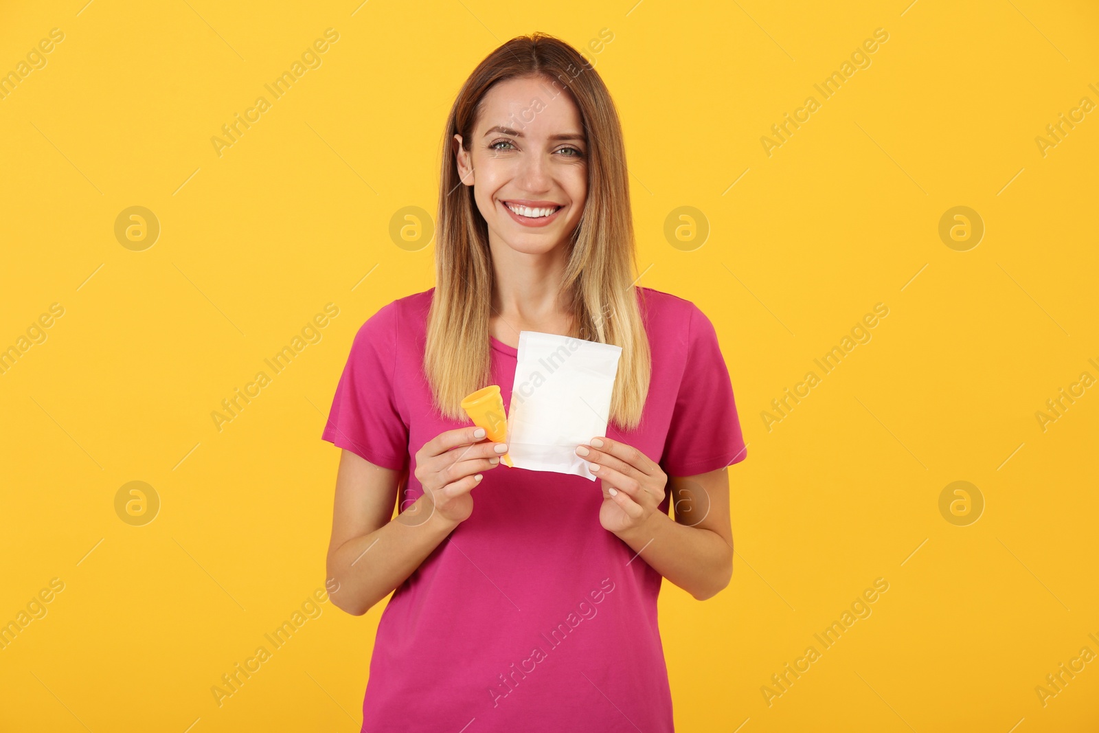 Photo of Happy young woman with menstrual cup and disposable pad on yellow background