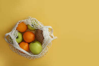 Photo of Net bag with fruits on yellow background, top view. Space for text