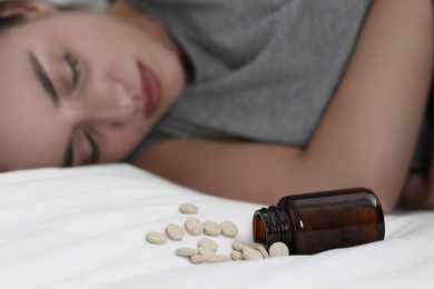Photo of Depressed woman sleeping on bed near overturned bottle with antidepressants, selective focus