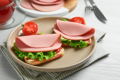 Plate of tasty sandwiches with boiled sausage, tomato and lettuce on white wooden table, closeup