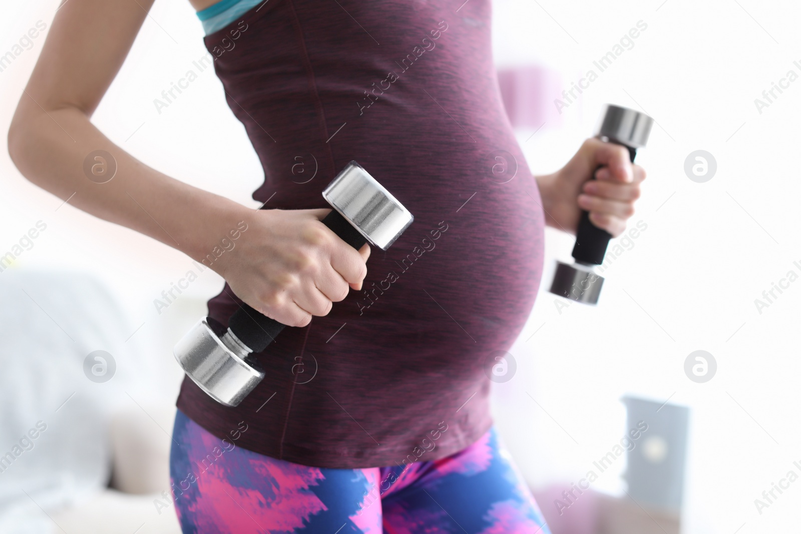 Photo of Young pregnant woman doing exercises with dumbbells at home