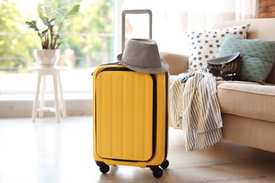 Bright yellow suitcase packed for journey and hat at home