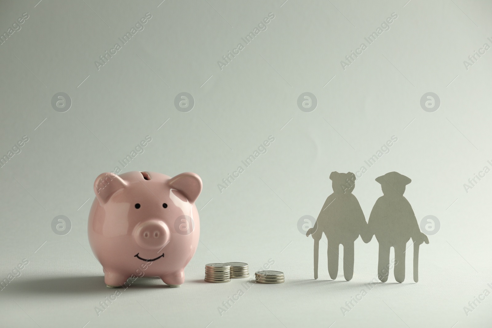 Photo of Pension savings. Figure of senior couple, piggy bank and coins on grey background