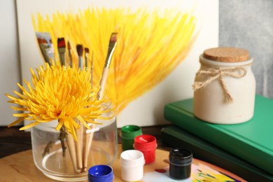 Canvas painting of chrysanthemum, flower, colorful paints and brushes on wooden table