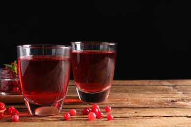 Photo of Tasty cranberry juice in glasses and fresh berries on wooden table. Space for text