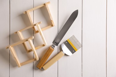 Photo of Honeycomb frames and beekeeping tools on white wooden table, flat lay. Space for text