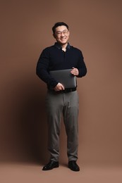 Full length portrait of happy man with laptop on brown background