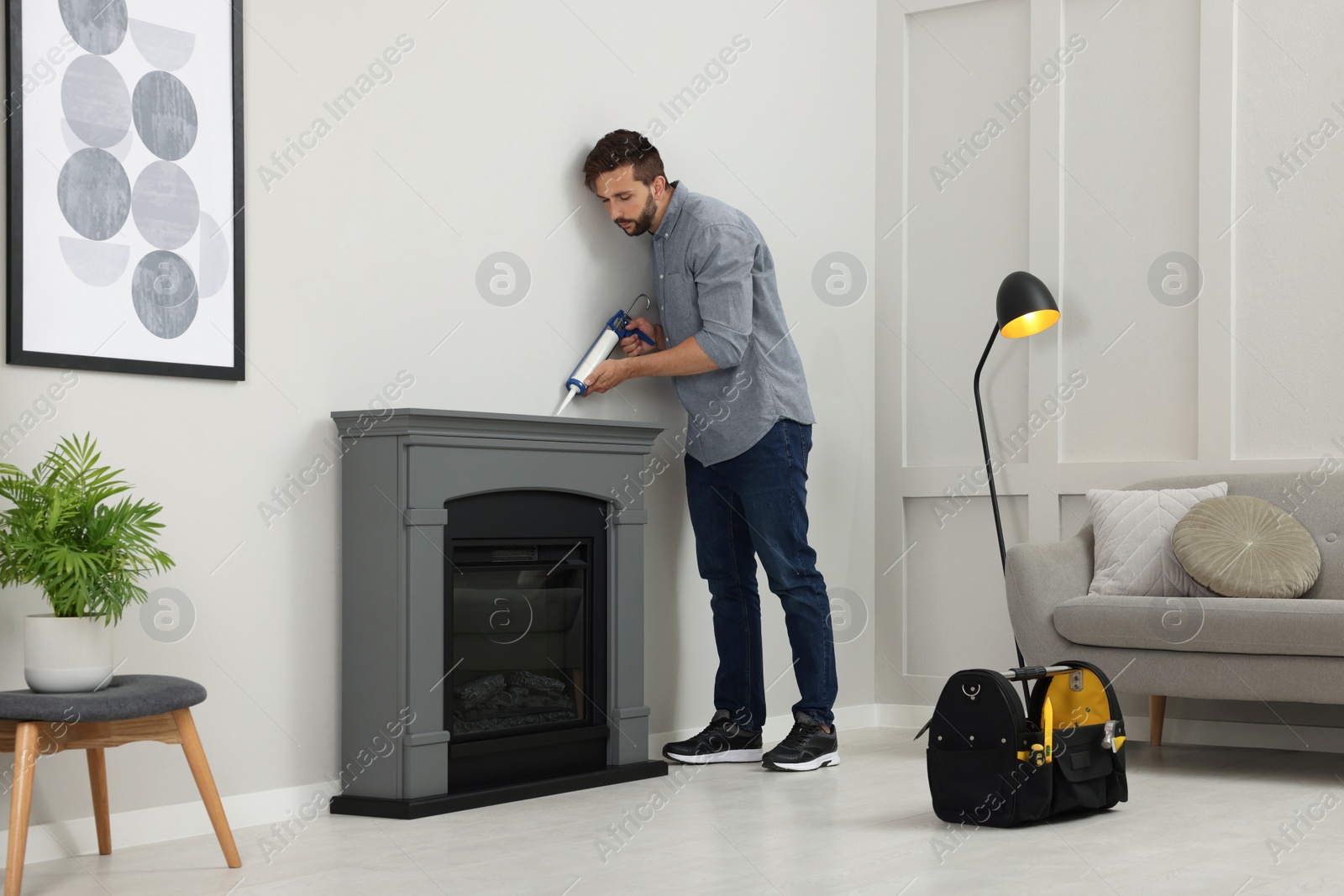 Photo of Man sealing electric fireplace with caulk near wall in room