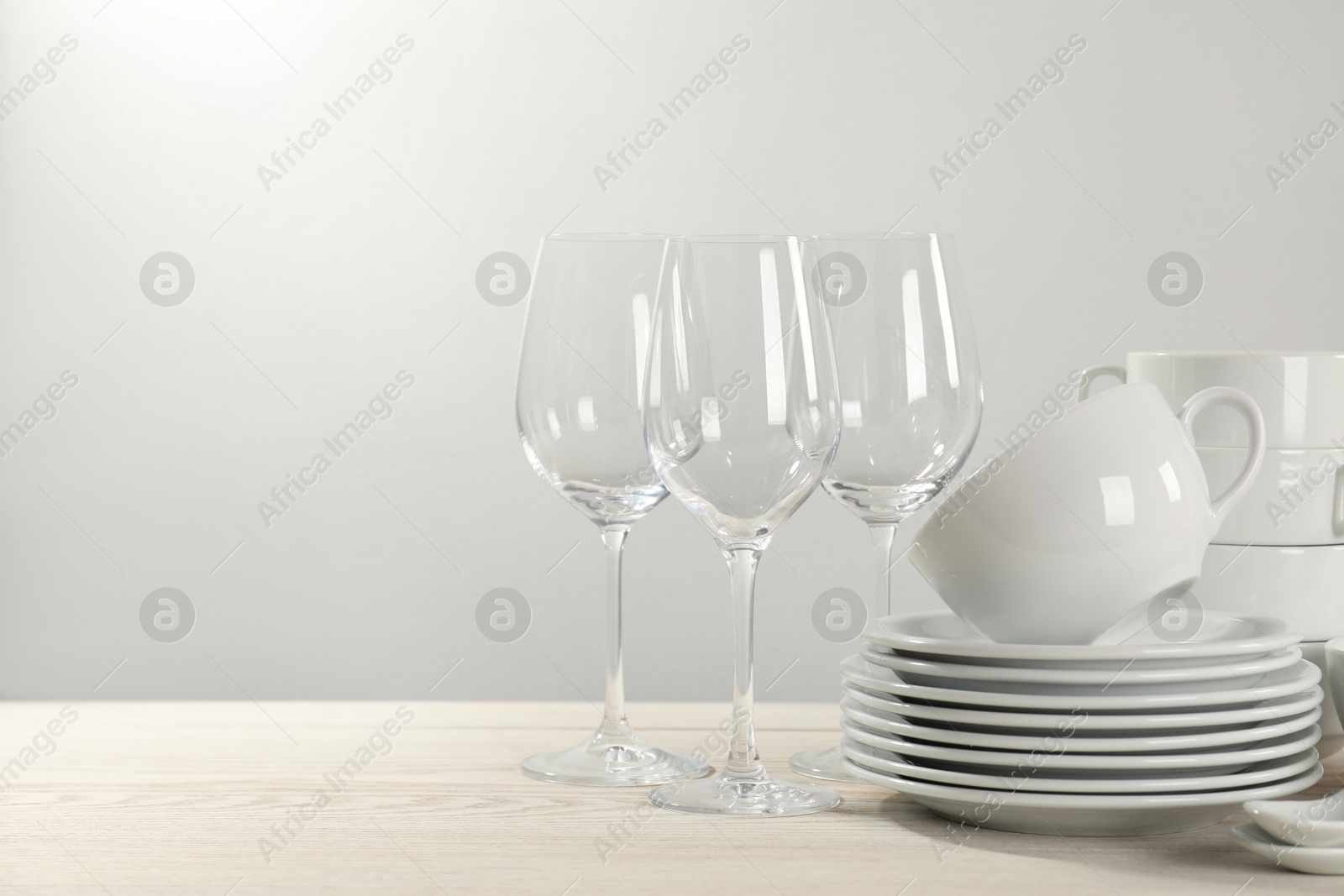 Photo of Set of clean dishware and glasses on white wooden table against light background. Space for text