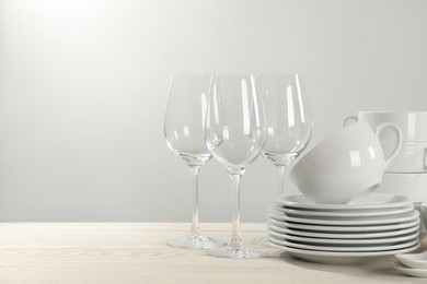 Set of clean dishware and glasses on white wooden table against light background. Space for text