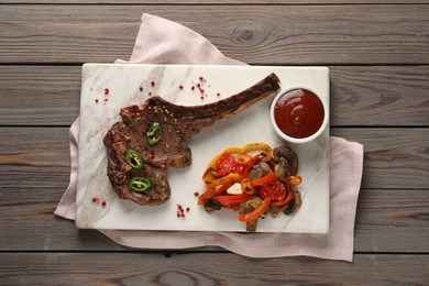 Delicious fried beef meat served with vegetables and sauce on wooden table, top view