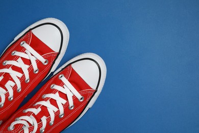 Photo of Pair of new stylish red sneakers on blue background, flat lay. Space for text