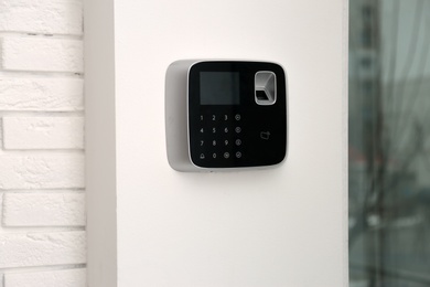 Photo of Modern alarm system with fingerprint scanner on white wall indoors