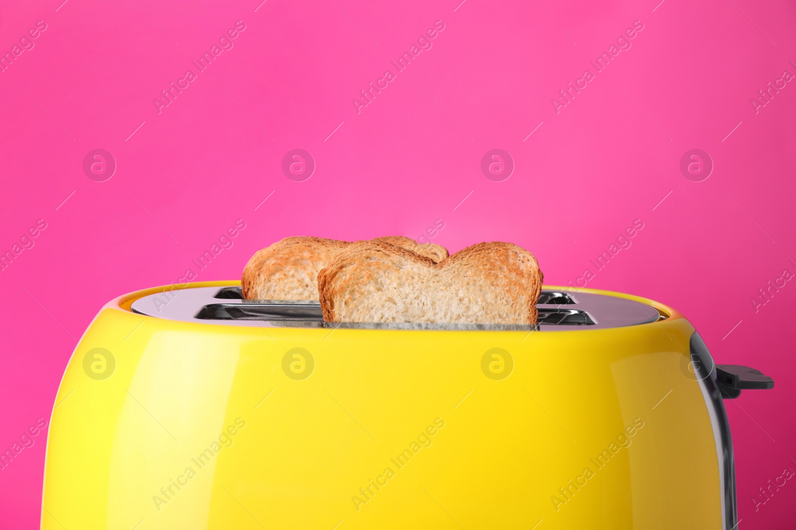 Photo of Yellow toaster with roasted bread against pink background, closeup