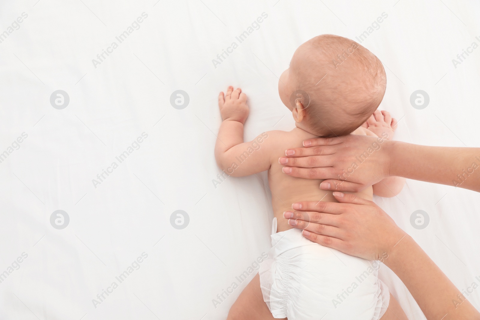 Photo of Top view of mother and her cute child on white bed, space for text. Baby massage and exercises