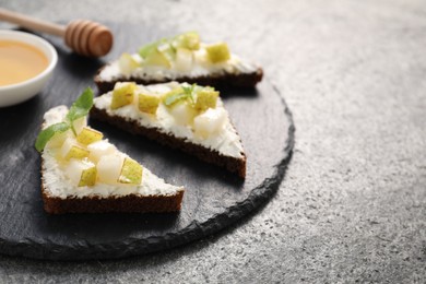 Delicious bruschettas with ricotta cheese, pear and mint on grey textured table, closeup. Space for text