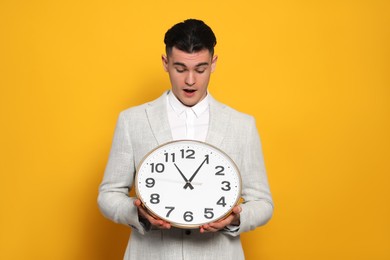 Emotional young man holding clock on orange background. Being late concept