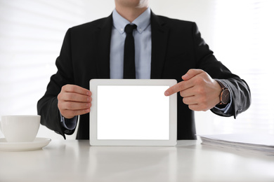 Businessman holding modern tablet with blank screen at white table in office, closeup