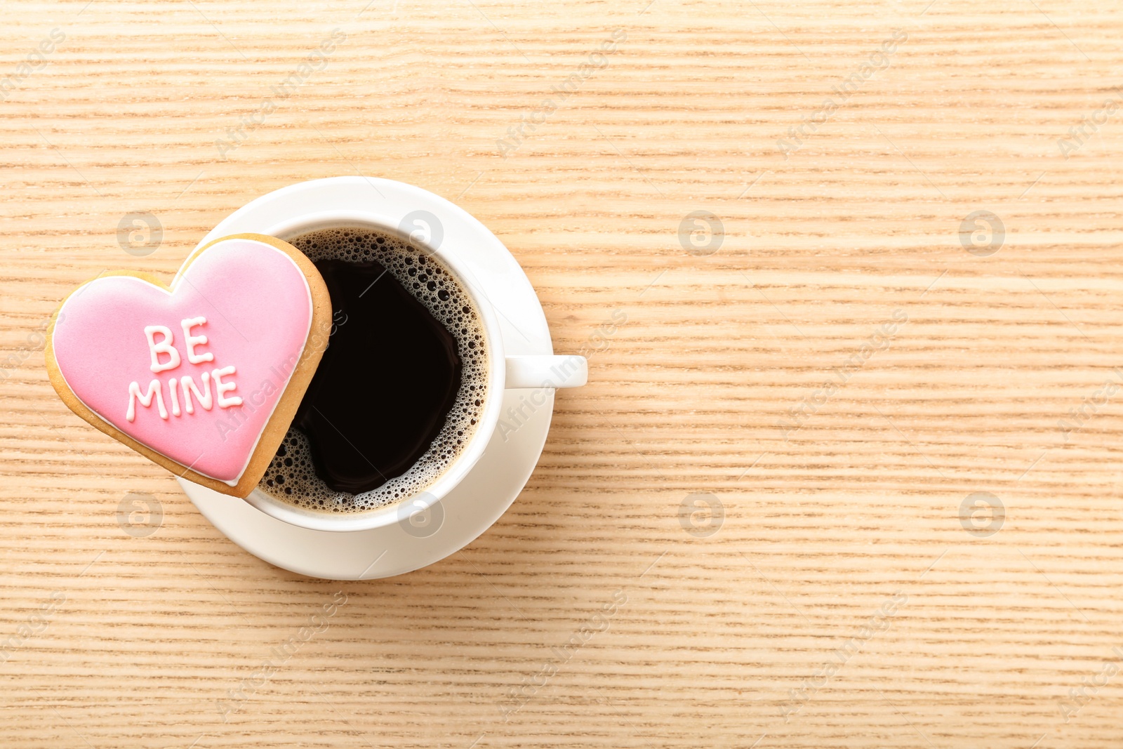 Photo of Heart shaped cookie with written phrase Be Mine and cup of coffee on wooden background, top view. Space for text